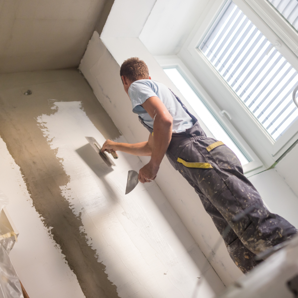 Plasterer in blue dungarees and t-shirt plastering a wall